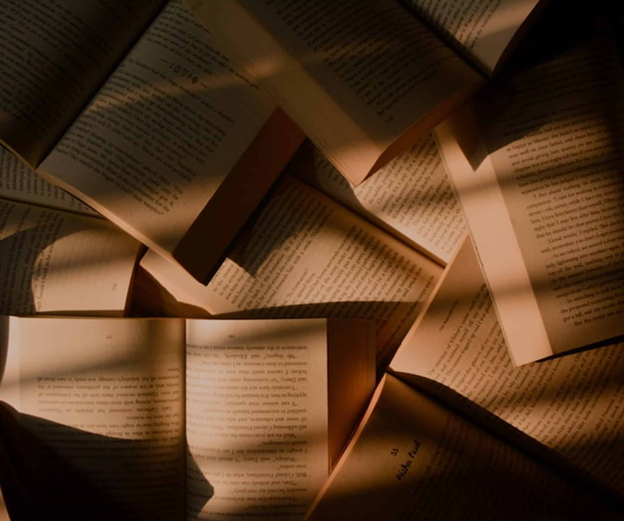 Plusieurs livres ouverts et éparpillés, leurs pages jaunies éclairées par des rais de lumière chaude sur fond sombre. Texte: "53 Aisha Paul".